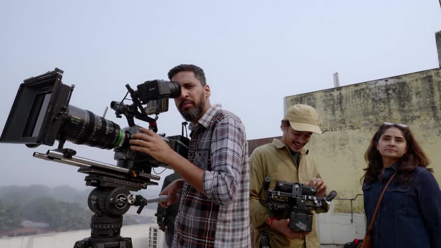 A film crew is shooting a scene with a camera on a rooftop