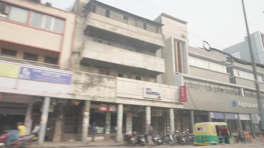 A street level view shows a row of weathered buildings with various storefronts and signage captured from a moving vehicle
