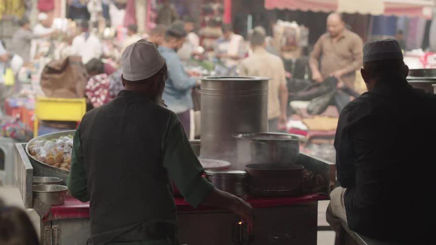 People are browsing the shops in the market as a vendor cooks