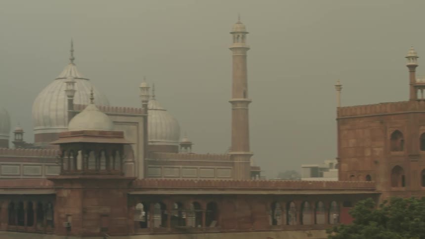An eyelevel shot shows the jama masjid in delhi featuring its domes minarets and arched entrances under a hazy sky