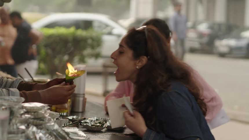 A woman eats a flaming novelty food served by an indian street vendor
