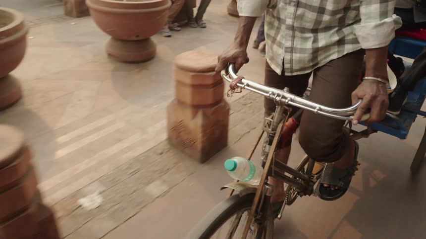 A person wearing sandals and dark pants rides a bicycle with a water bottle attached passing a wooden bollard on a paved surface
