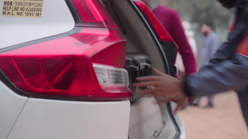 A person places a black case into the open trunk of a red and white vehicle