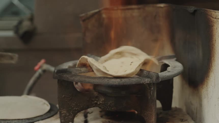 A piece of unleavened flatbread is being cooked directly over an open gas flame on a stove