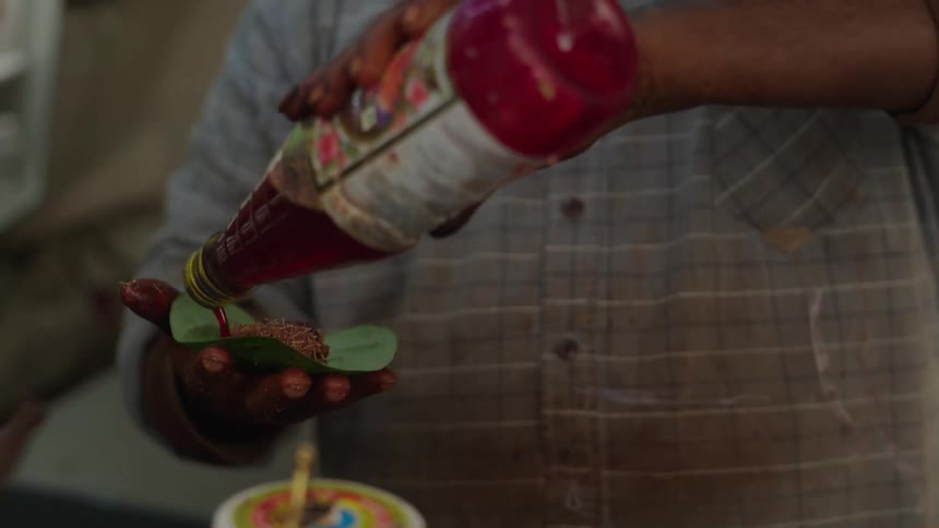 A closeup shows a vendor preparing a dish using a large leaf as the plate with sauce and condiments being added