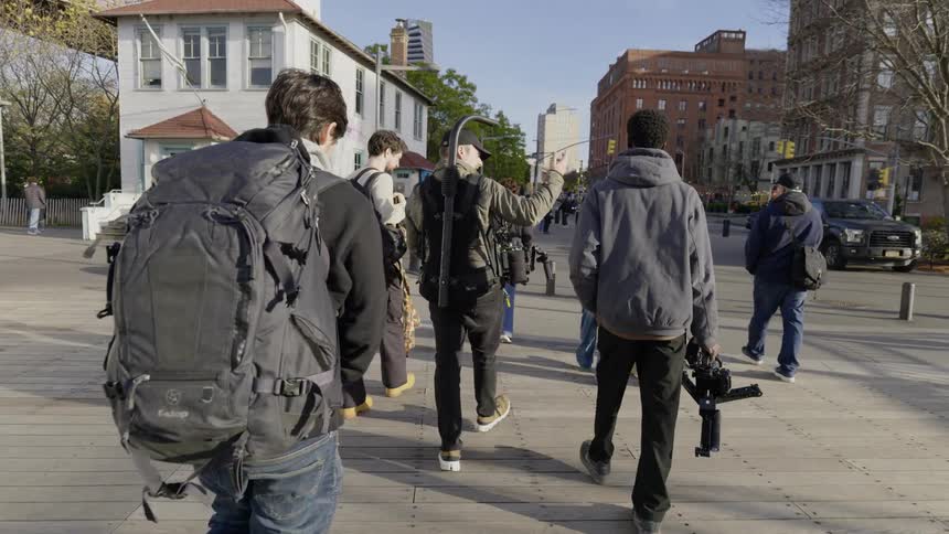 A film crew carries their equipment on the sidewalk