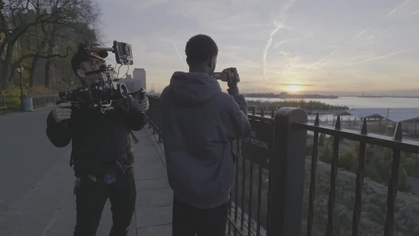 Filmmaker filming another man with a small camera filming the sunrise on the horizon