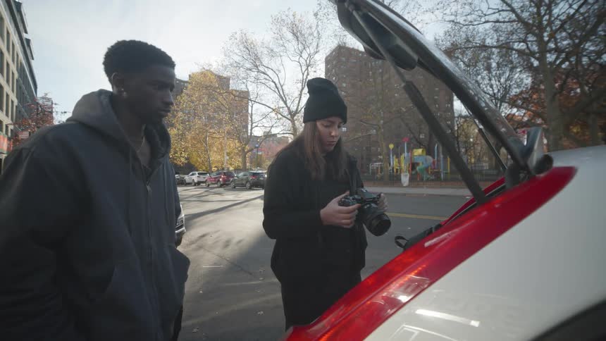 A woman is looking at a camera by her car