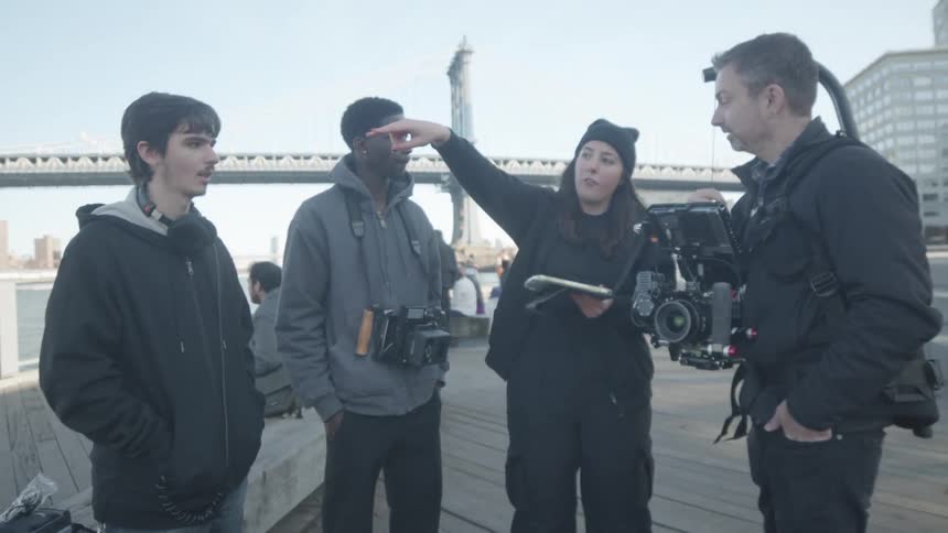 Members of a film crew hold a discussion while standing on the boardwalk across the river from downtown on a cold day