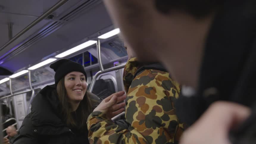 Two people talking on a subway one wearing a camouflage jacket and the other a black beanie