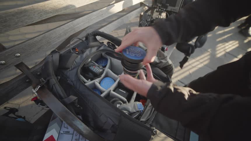 Filmmaker taking lens of a professional camera from a backpack with equipment