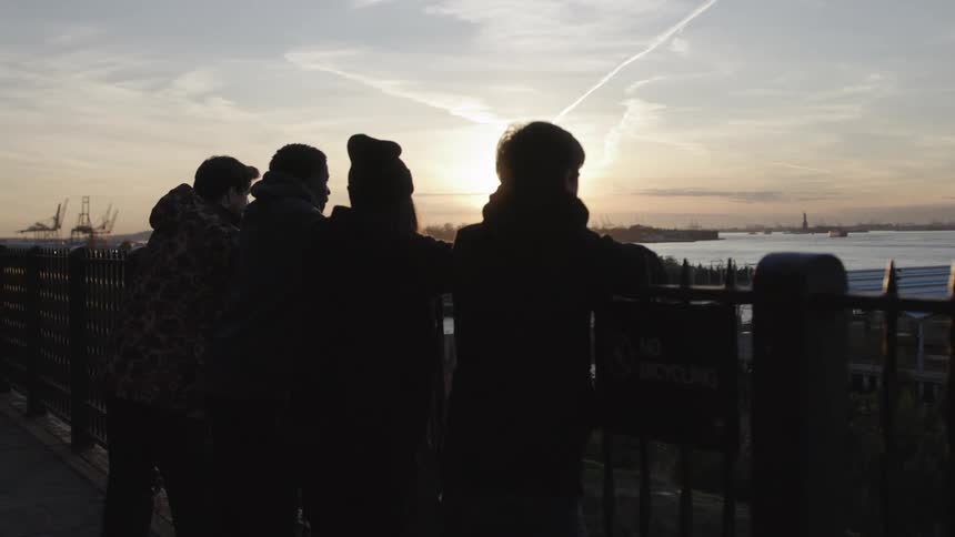 Four people stand at a railing overlooking a body of water at sunset