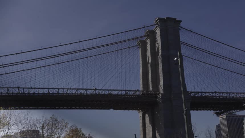 A lowangle shot shows the stone pylons and intricate cable network of the brooklyn bridge against a clear dark blue sky
