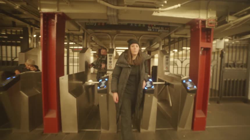 Woman and a man with a professional video camera walking through the turnstile of an underground metro station