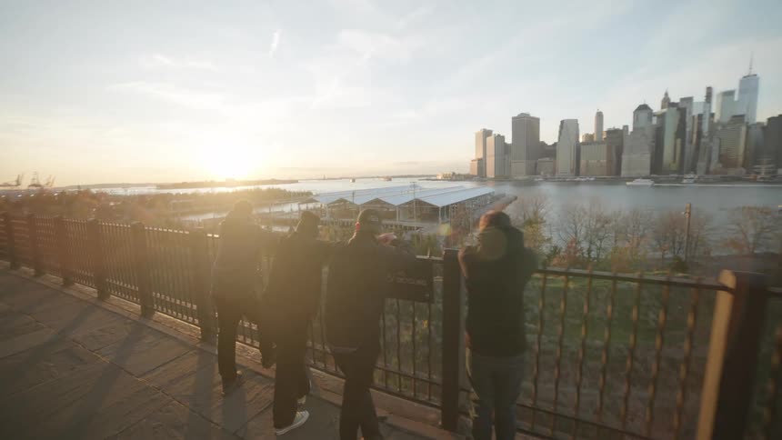 Four people leaning against a metal fence enjoying the view of a metropolis with skyscrapers by the sea
