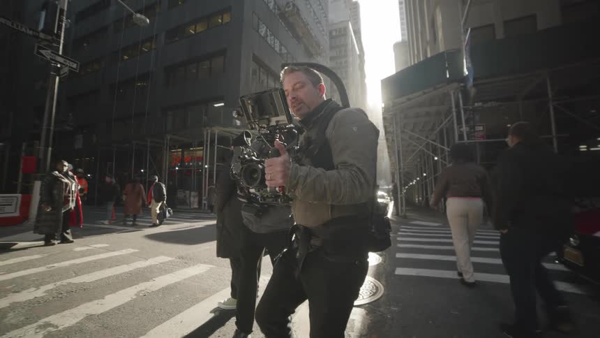 A film crew working on a busy city street with the sun casting long shadows