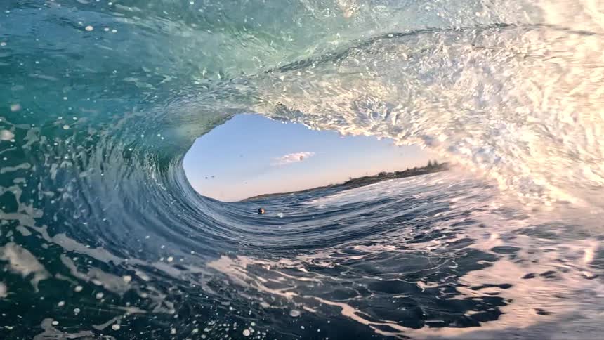 Surfer rides through the barrel of a collapsing wave on a sunny day