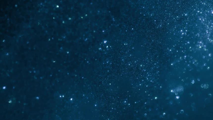 A closeup of a swirling mass of glittering specks suspended in a thick blue liquid