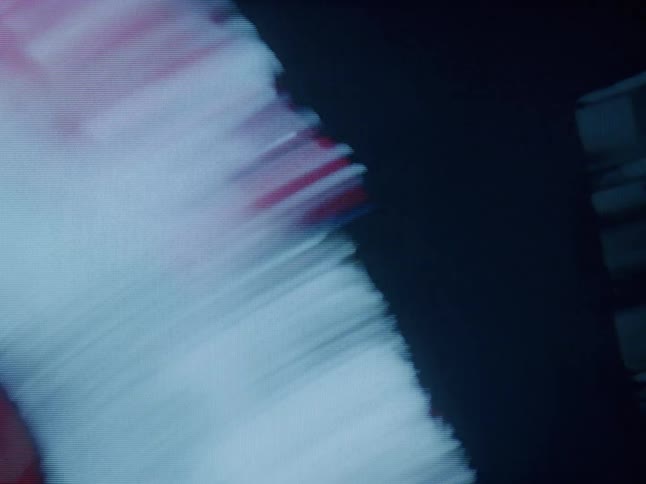 A grainy stylized shot of a woman with short dark hair facing away from the camera against a deep red background with a double exposure creating an abstract layered visual
