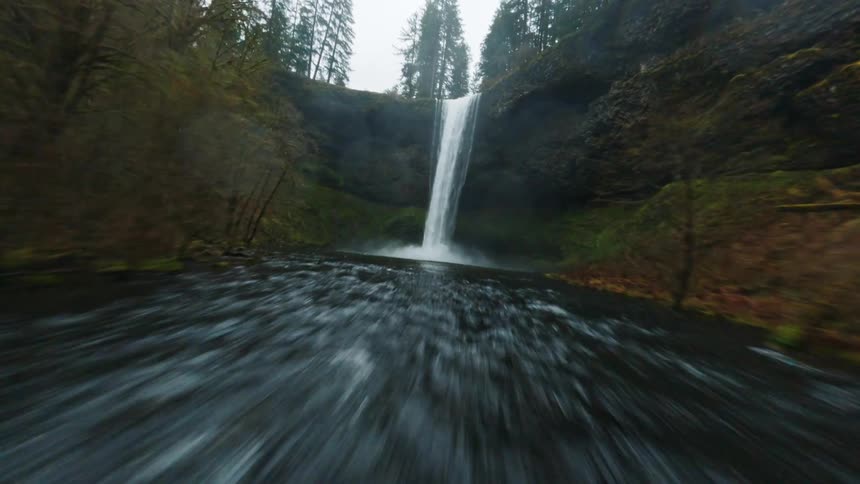 People stand on the bridge crossing a river fed by a waterfall on an autumn day