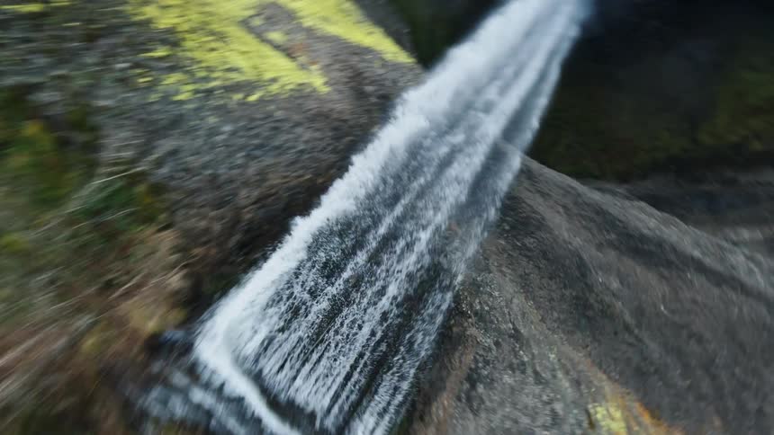 A waterfall goes over a cliff and drops to a river surrounded by trees
