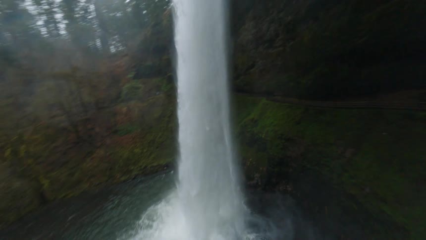 A tall narrow waterfall plunges into a dark pool at the base of a mossy cliff