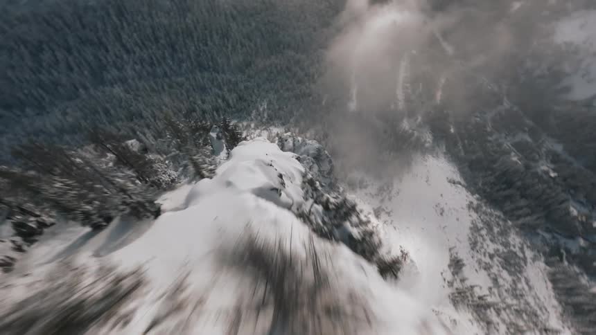 Aerial view of a snowcovered mountain ridge with steep cliffs and a dense forest below partially shrouded in mist