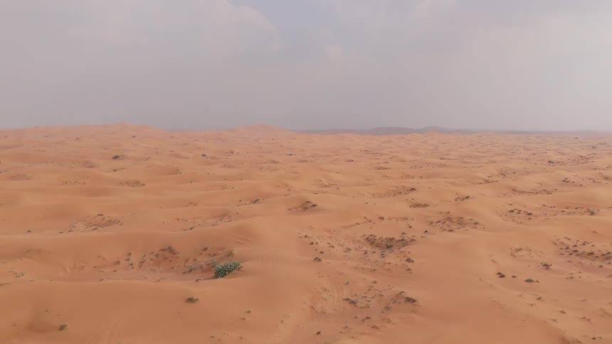 Mounds of sand form dimples across a barren desert terrain under a clouded purplegray sky