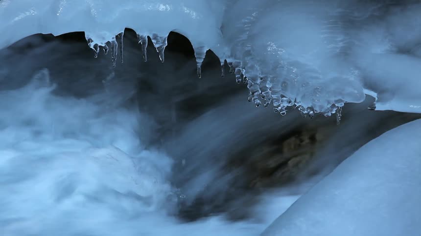 Water in a stream rushes beneath an ice ledge