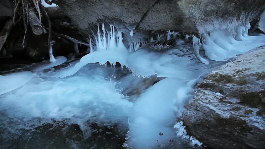 Water in a stream is flowing beneath ice and between rocks
