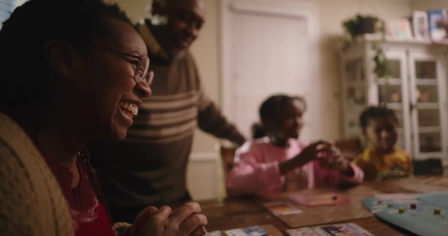 A family gathers around a dining table at home playing a board game together