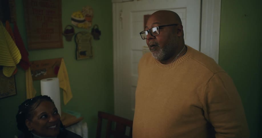 Man standing next to a woman who is sitting at a table talking