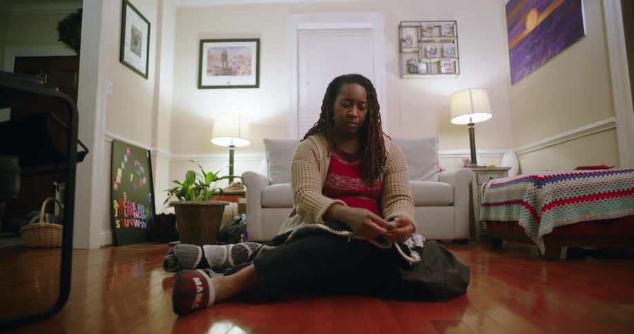 A woman sits on the floor of a modern living room hand sewing a piece of garment