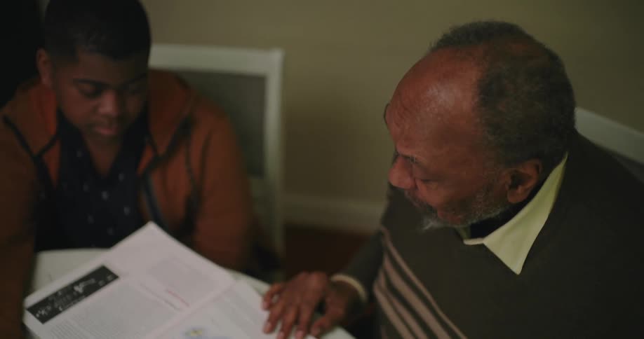 A man is reading from a textbook to his grandson