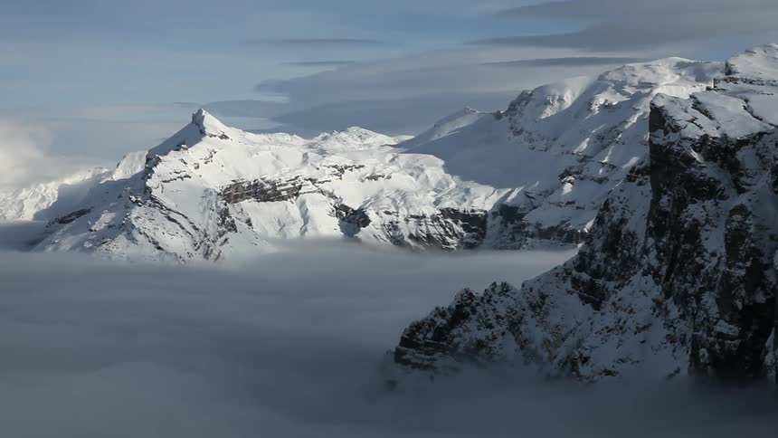 Snow covered mountain tops sticking out of thick clouds