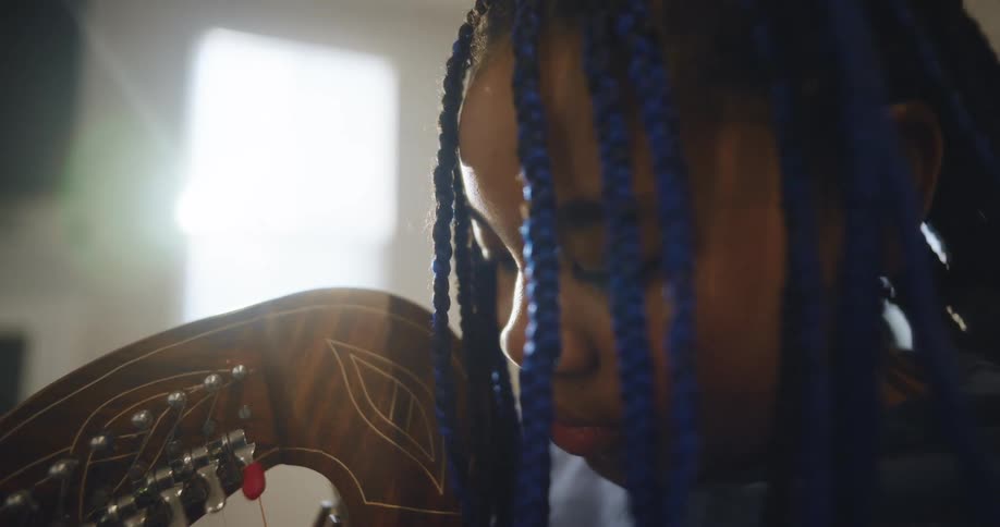 The young girl with the blue braids is playing an instrument that only a small section is visible on