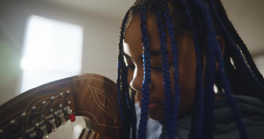 Close up of a girl with braided hair playing the harp on a well lit room