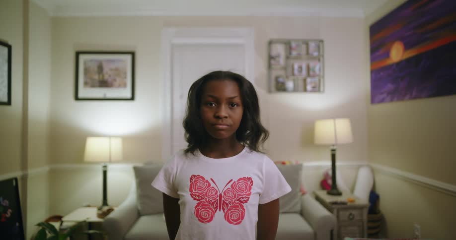 A girl stands on a modern living room looking at the camera