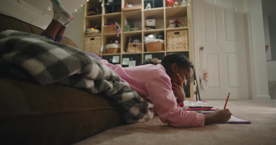 A teen girl is drawing in a notebook while on the living room couch