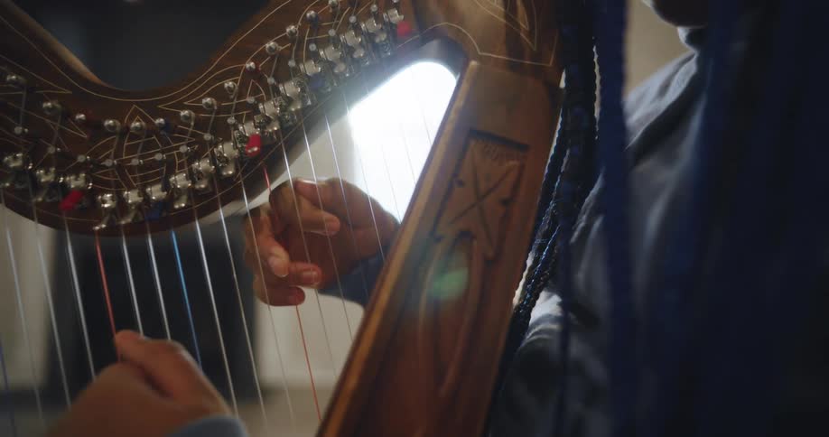 A persons hands gently plucking the strings of an intricately decorated harp