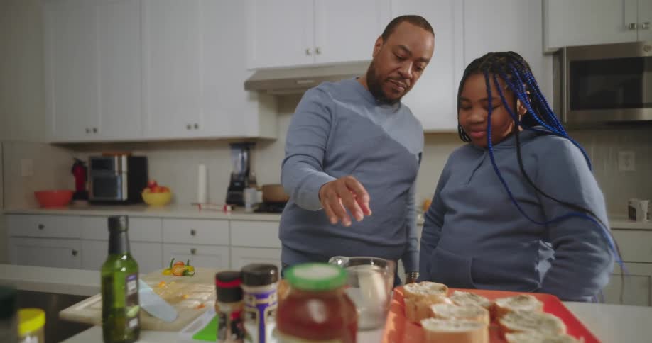 A father and his teenage daughter cooking together in the kitchen at home