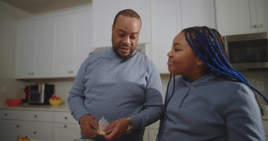 A father is preparing food in a kitchen as he talks to his daughter