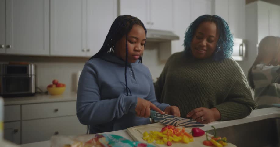 Mother watching her daughter cutting vegetables in the kitchen