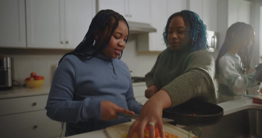 A family is in the kitchen cutting ingredients and cooking a meal together