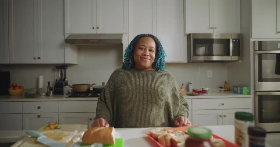 A woman with blue hair stands in a modern kitchen preparing food on a counter