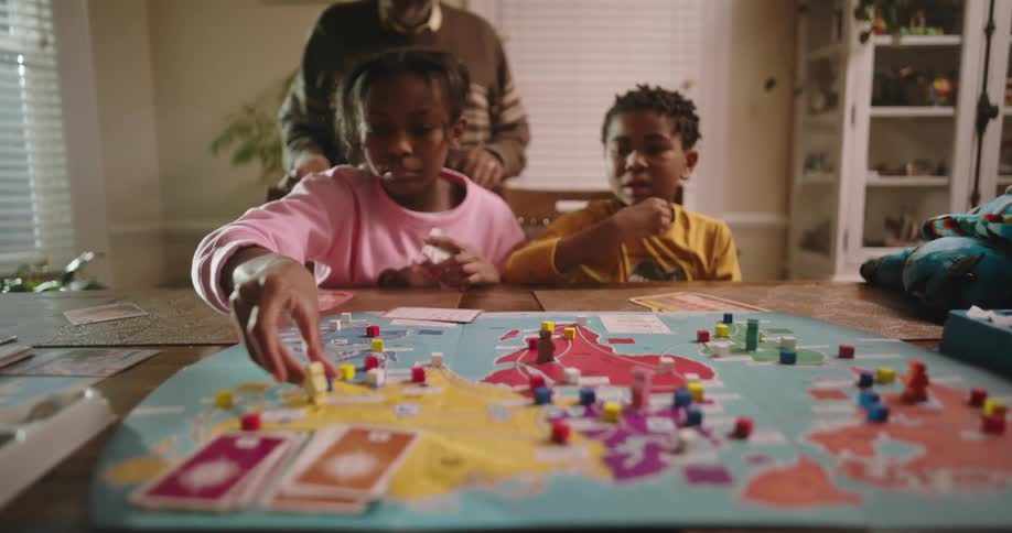 Two children accompanied by an elderly man playing a board game on the table