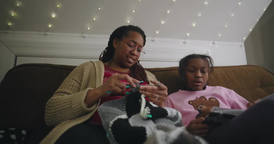 Mother crocheting while listening to her daughter read a book