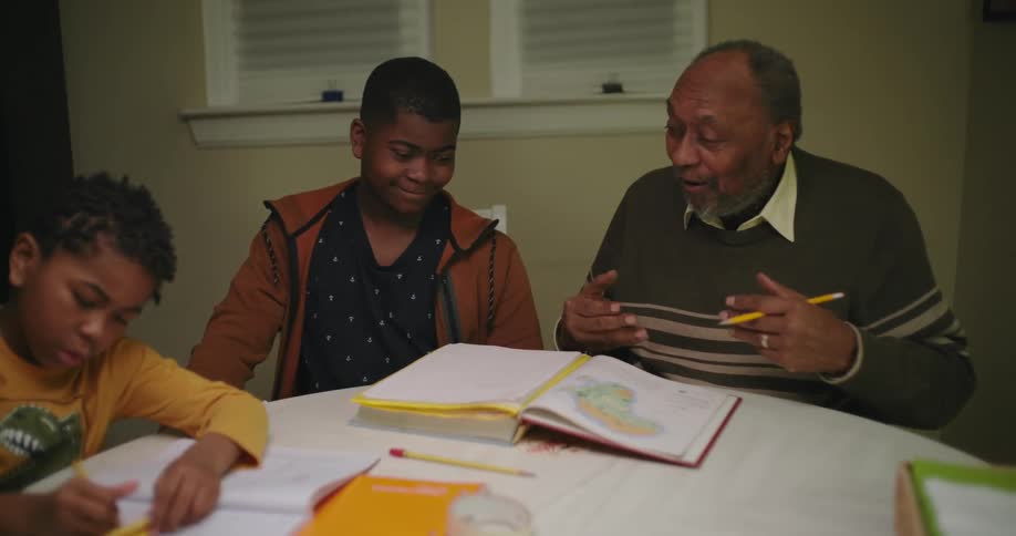 Grandfather sitting at the table studying with his two grandchildren with books open