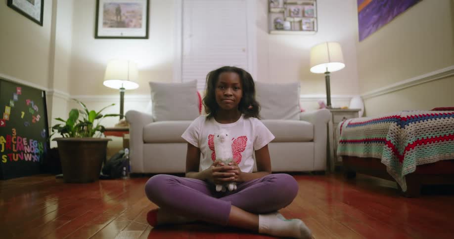 A girl sits on the wooden floor of a well lit modern living room