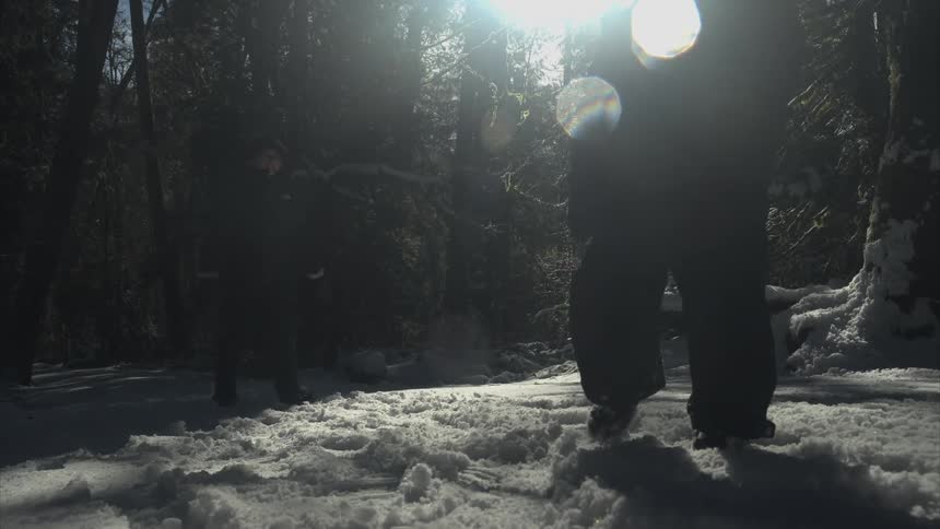 A little girl kicks the snow as she walks in a forest with her mom